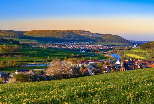 Bild in den Abendstunden mit Blick auf Ortschaften entlang der Donau mit grünen Wiesen und Feldern und blauem Himmel im Hintergrund der leicht rötlich gefärbt ist.