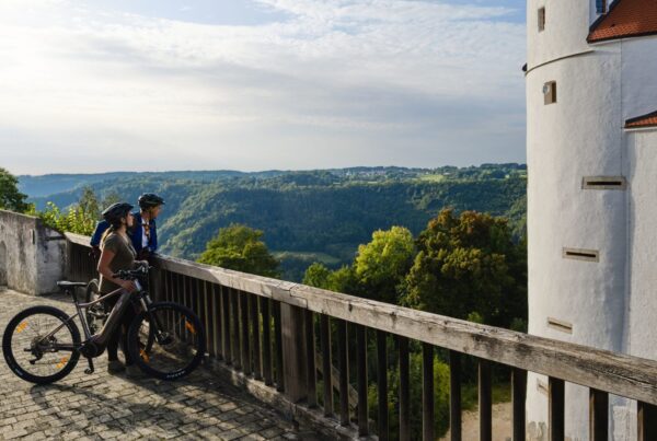 Themenbild mit zwei Radfahrern, die am Geländer vor Burg Wildenstein in die Natur schauen