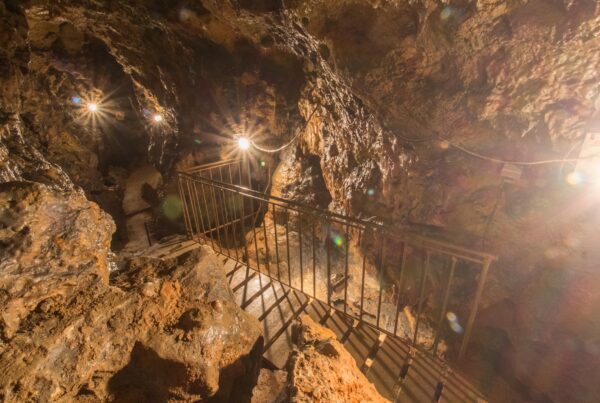 Bild von der Felsenhöhle von Innen mit einem beleuchteten Weg auf Holzdielen an einem Eisengeländer entlang