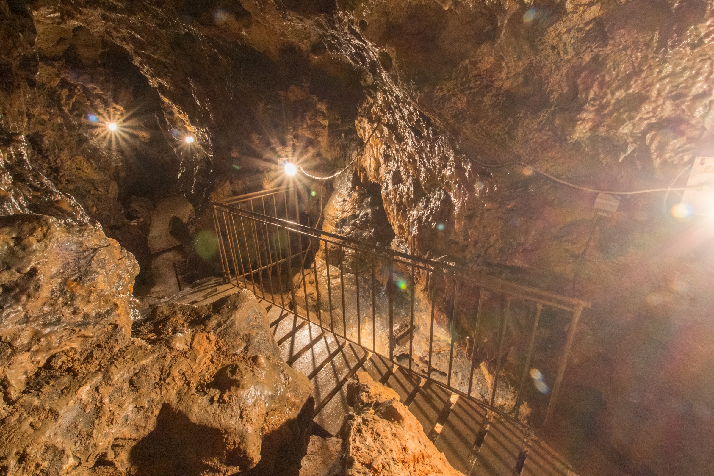Picture of the rock cave from the inside with an illuminated path on wooden planks along an iron railing