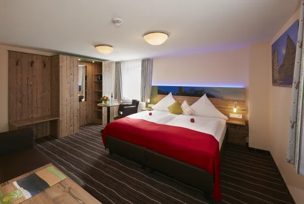 Bild von einem Hotelzimmer mit Bett, Ablagefläche, Regalen und kleinem Tisch und Stuhl