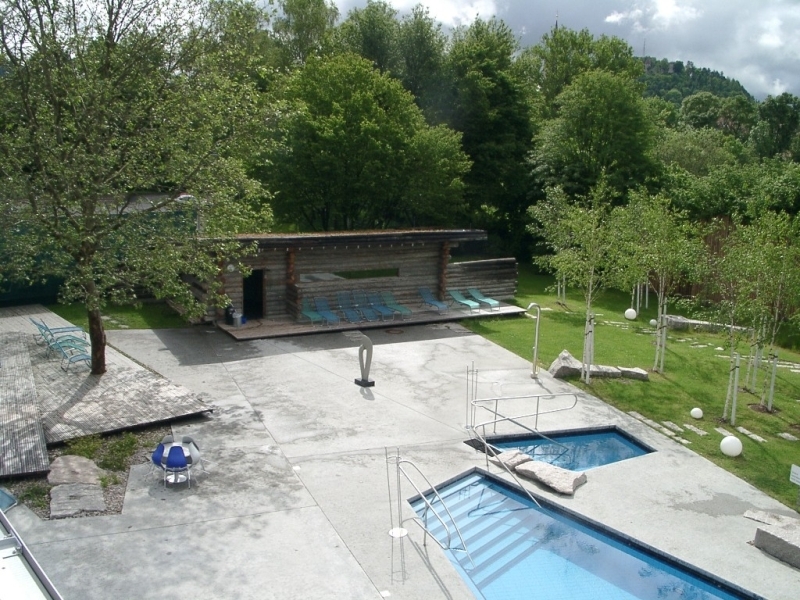 Bild von der Außensauna im Tuwass von oben fotografiert mit Liegewiese, Liegestühlen und zwei Tauchbecken in Beton eingefasst und von Bäumen umgeben