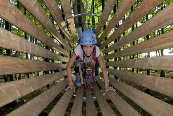 Bild von einem Kind in einer Holzröhre mit Kletterausrüstung im Hirscherlebniswald in Mahlstetten