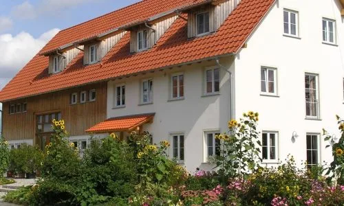 Bild vom Landhotel Brigel Hof mit Putz- und Holzfassade und einem Blumenbeet mit rosa und gelb blühenden Blumen