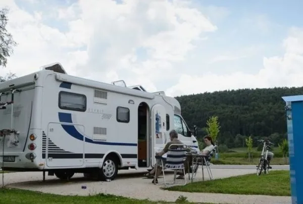Bild von einem Camper auf dem Reisemobilstellplatz in Geisingen. Zwei Personen sitzen neben Ihrem Camper und lesen. Der Himmel ist bewölkt