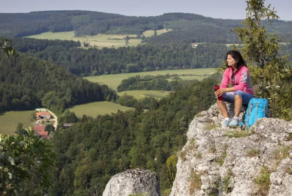 Bild einer Wanderin, die auf einem Felsen sitzt und in die Landschaft schaut